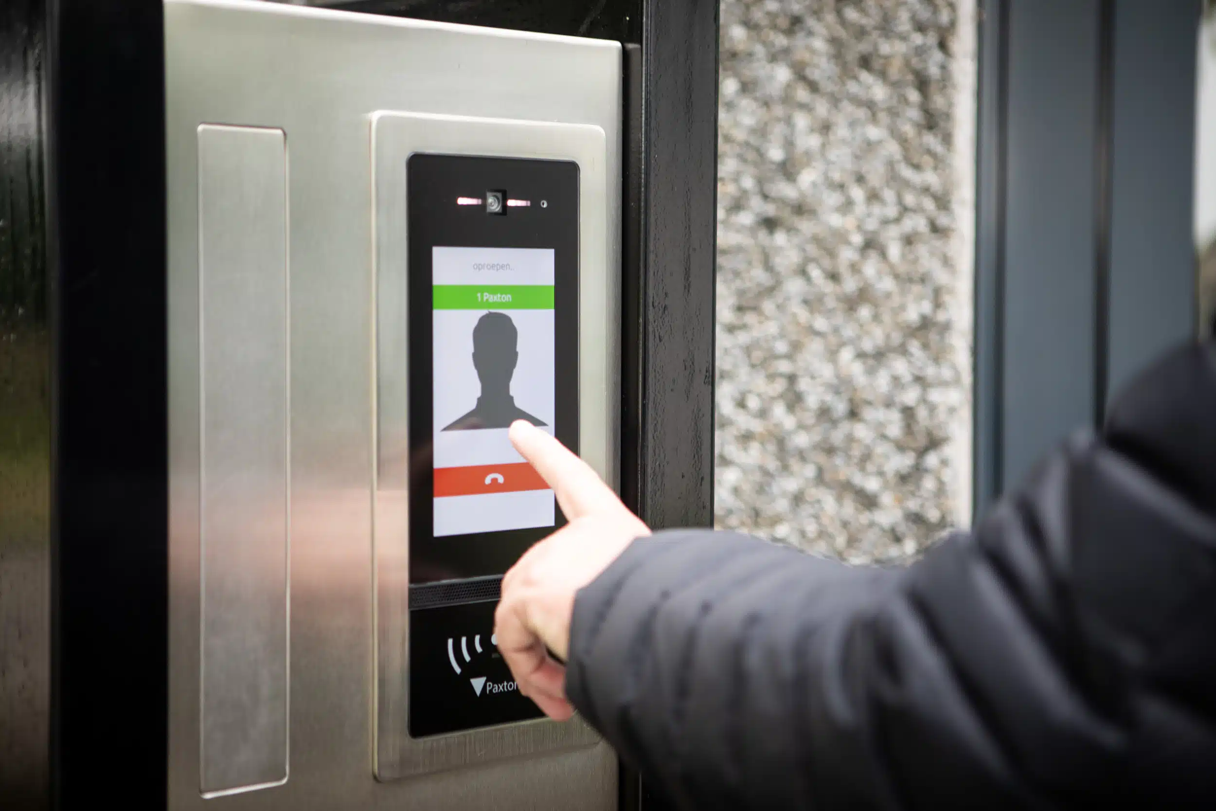 Persoon gebruikt interactief touchscreen voor toegangsverificatie bij een Paxton toegangscontrolesysteem, een veilige en moderne oplossing van Meuleman voor gecontroleerde toegang.
